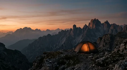 Tenda illuminata al tramonto sulle montagne italiane durante un bivacco notturno