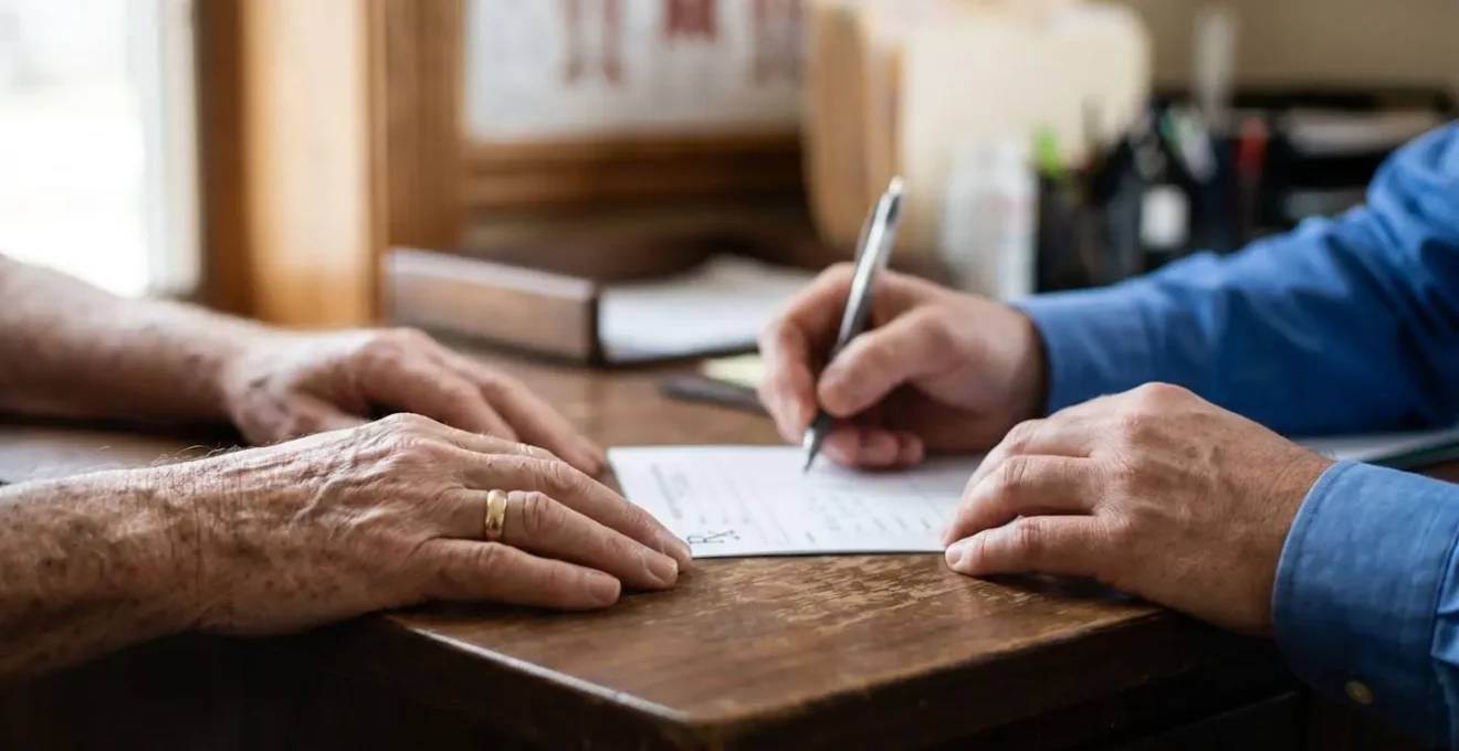 Primo piano delle mani di un medico che compila una prescrizione per cure termali mentre discute con un paziente anziano