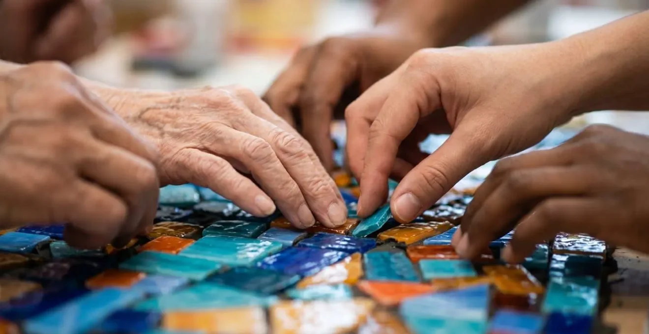 Mani diverse che posizionano piccole tessere di mosaico per formare un'opera d'arte collettiva