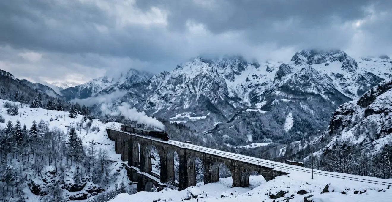 Treno storico a vapore che attraversa un viadotto innevato tra le montagne abruzzesi